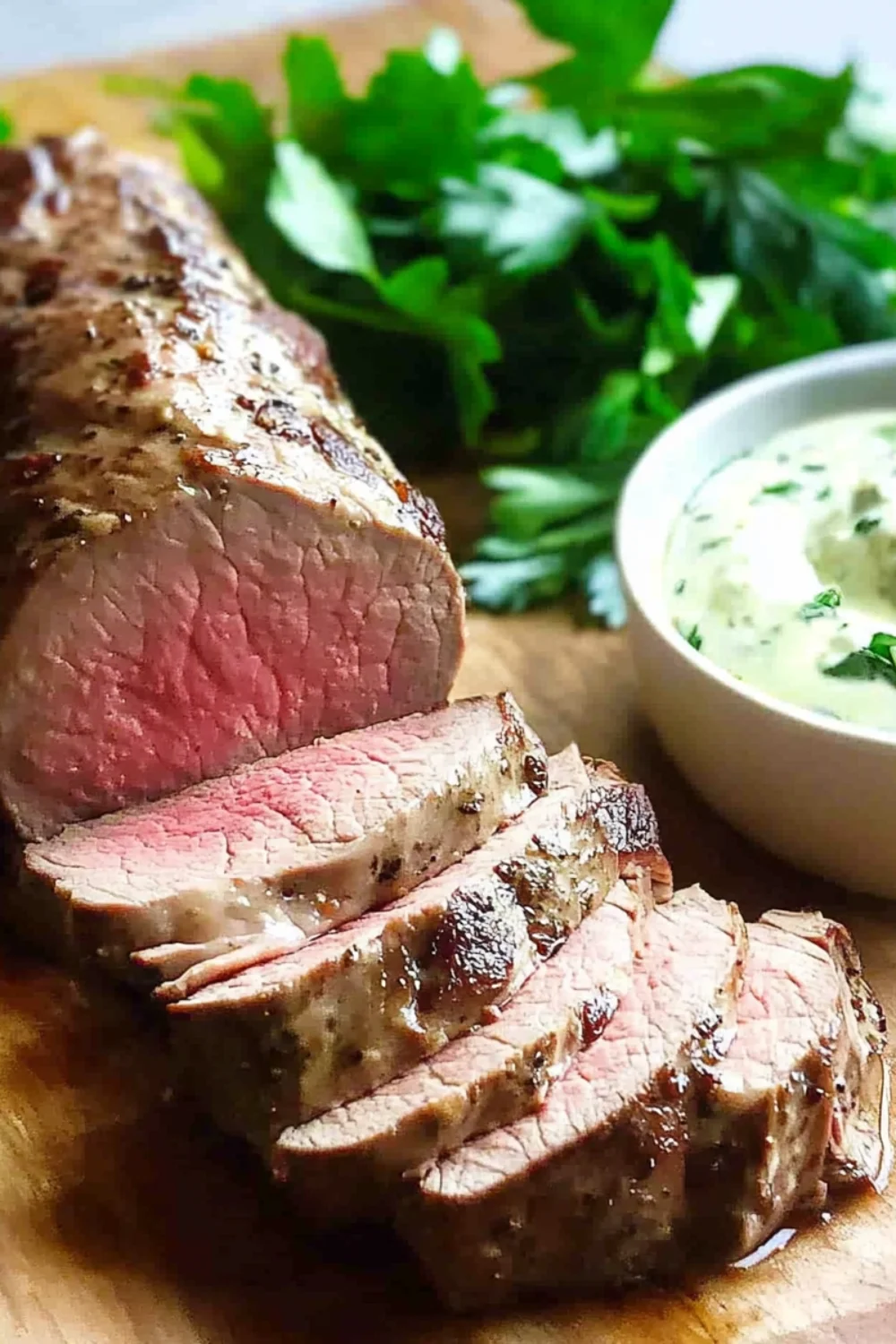 Zartes, perfekt gegartes Schweinefilet, das in dicke, saftige Scheiben geschnitten wurde, serviert mit einer grünen Kräutersoße und frischen Kräutern.