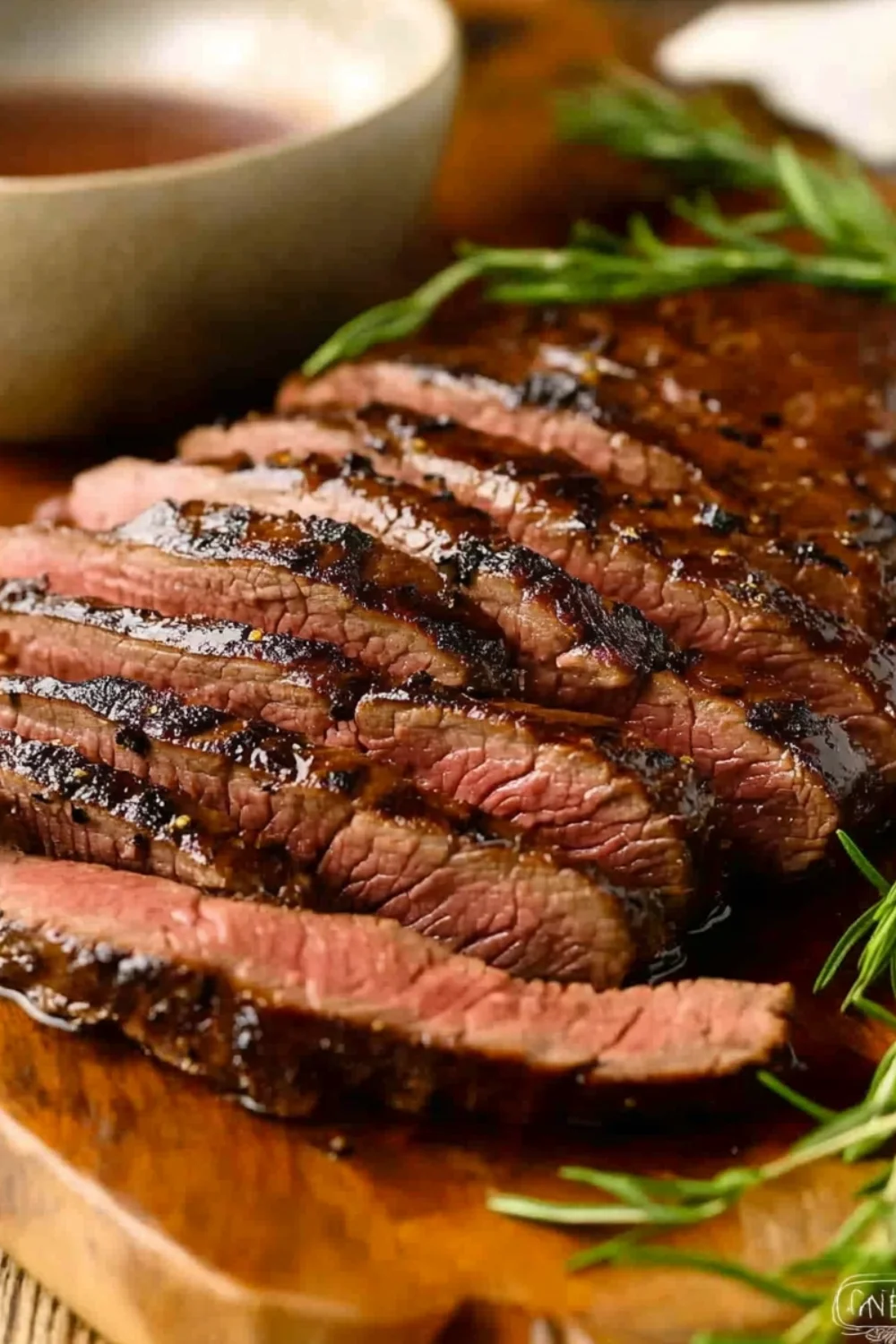 Saftig gegrilltes Steak in perfekt geschnittenen Scheiben, serviert auf einem Holzbrett, mit Rosmarinzweigen und einer Beilage Sauce.