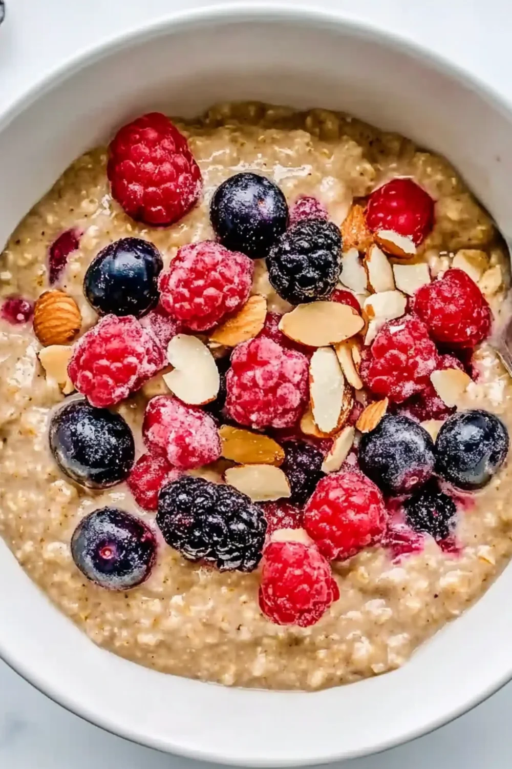Schüssel mit Haferflocken, garniert mit frischen Beeren und Mandelscheiben.