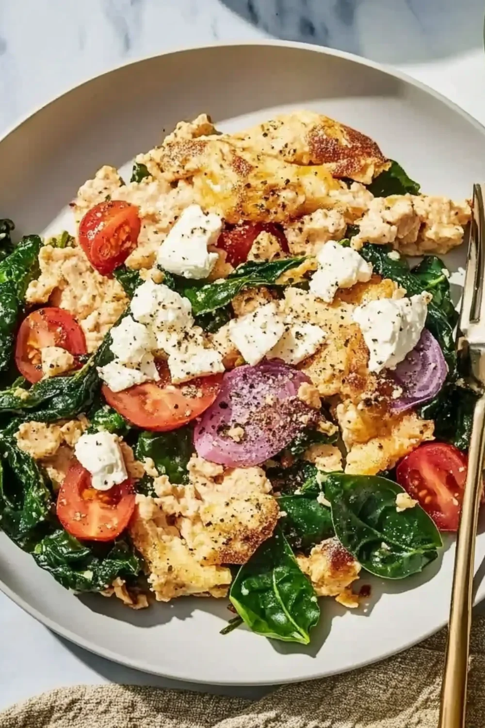 Rührei mit Spinat, Tomaten, roten Zwiebeln und Feta auf einem Teller.