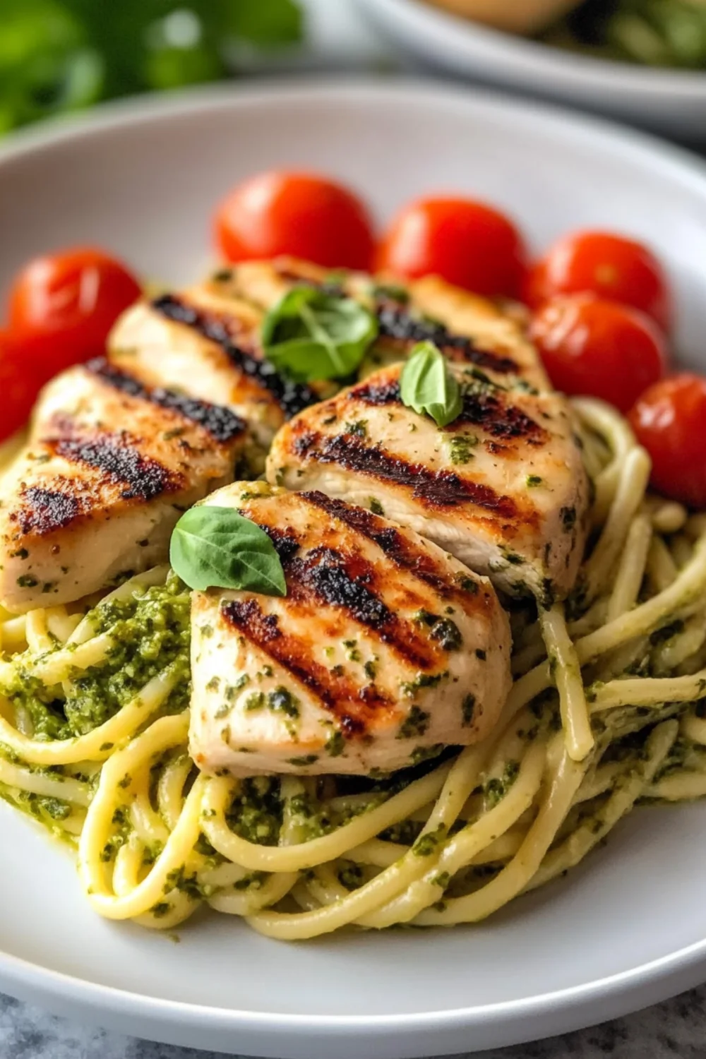 Gegrilltes Hähnchenfilet auf Pesto-Pasta, garniert mit frischen Tomaten und Basilikumblättern.